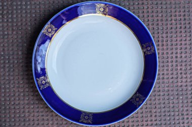 bir beyaz boş seramik tabak ile bir renk deseni ve mavi kenar kahverengi masa üzerinde duruyor