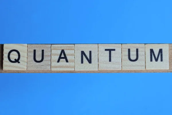 stock image word quantum made from wooden gray letters lies on a blue background