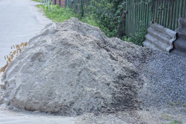 Gri asfalt üzerinde beyaz kum ve gri moloz yığını cadde üzerindeki çitin yanında.