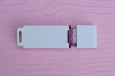 Pembe ahşap bir masada duran küçük, beyaz plastik, kapalı bir taşınabilir bellek.