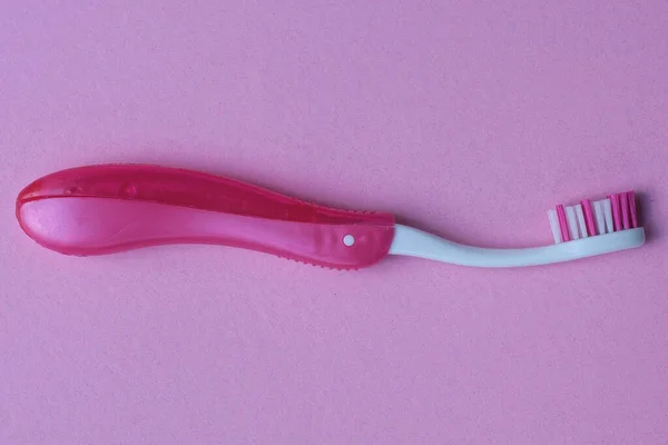プラスチック製の赤い白い歯ブラシがピンクのテーブルの上にあり — ストック写真