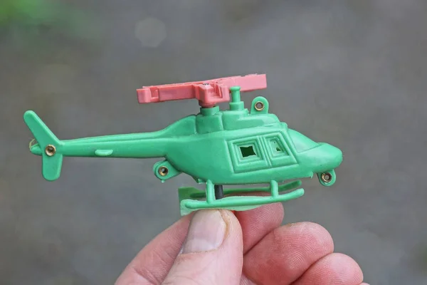 Palce Trzymające Małą Zieloną Plastikową Zabawkę Śmigłowca Zewnątrz Szarym Tle — Zdjęcie stockowe