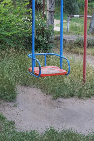 一个空的摇椅 用蓝色的金属和红色的木板做的 靠在绿草的背景上 — 图库照片