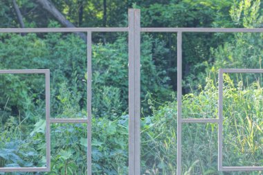 Sokaktaki yeşil çimlerde demir parmaklıklardan yapılmış gri metal bir çitin parçası.