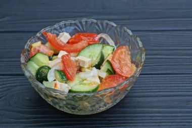 Salata, salatalık, salatalık ve soğan karışımı siyah ahşap bir masada cam bir kasede.