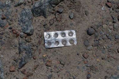 İlaçlar için boş beyaz plastik bir paketin çöpleri sokaktaki kumda yatıyor.