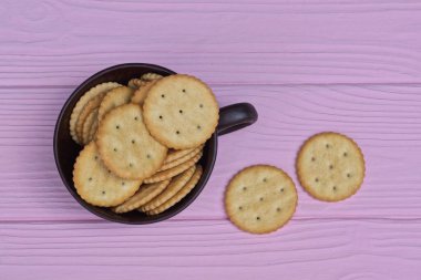 a pile of brown round cookies in a cup stands on a pink wooden table