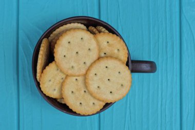 Bir fincandaki kahverengi yuvarlak kurabiye yığını mavi ahşap bir masada duruyor.