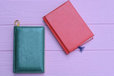 İki kapalı kırmızı ve yeşil deri defter pembe bir masanın üzerinde.