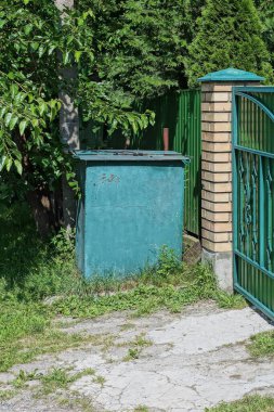 Bir yeşil kapalı metal çöp tenekesi sokakta çitin duvarında duruyor.