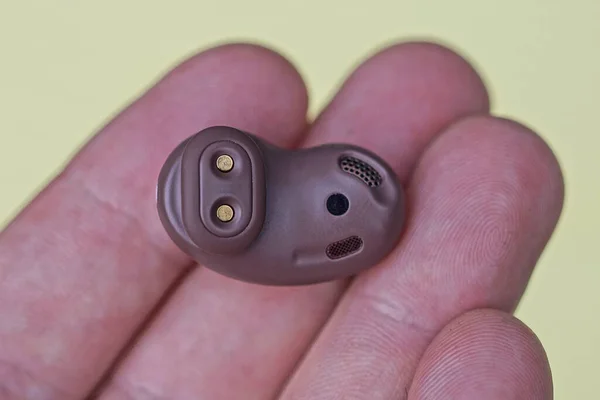 One Small Brown Plastic Wireless Headphone Lies Fingers Hand Yellow — Stock Photo, Image
