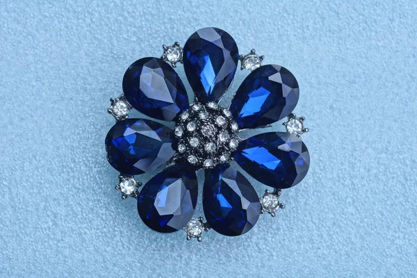 白いテーブルの上に青い石の花の形をした丸い銀の宝石のブローチ — ストック写真
