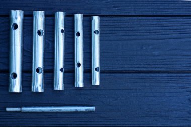 Bir dizi gri metal boru anahtarı siyah ahşap bir masanın üzerinde duruyor.