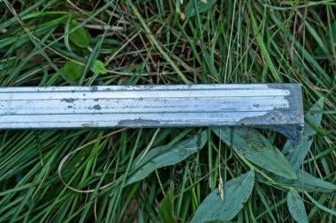 Gri alüminyum bir profil sokaktaki yeşil çimlerde yatıyor.