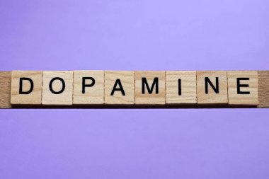 Dopamin kelimesi ahşap gri harflerden yapılmıştır. Leylak arkaplanda yatar.