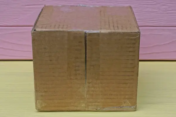 Jeden Brązowy Papier Zamknięty Kwadratowe Pudełko Kartonowe Leży Żółtym Drewnianym — Zdjęcie stockowe