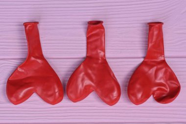 Pembe ahşap bir masada üç adet kırmızı lastik top duruyor.