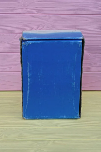 一只蓝色长方形纸盒放在一张黄色的木制桌子上 靠着粉红的墙壁 — 图库照片