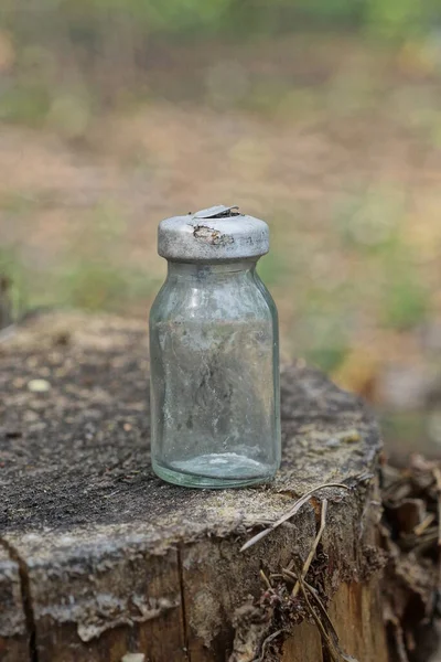 one small glass bottle vial with a aluminum white cap stands on a gray wooden stump in nature in the forest