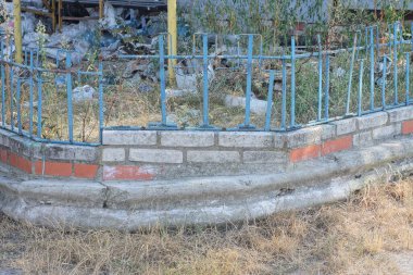 Kırsal bir sokakta beyaz bir tuğla temeli üzerine demir parmaklıklardan yapılmış mavi eski metal bir çitin parçası.