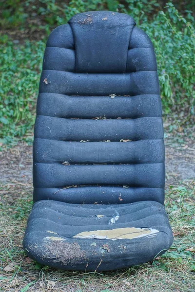 引き裂かれた生地が付いている古い黒い汚れたコンピュータの椅子は夏の公園の屋外の地面そして緑の草の上にあります — ストック写真