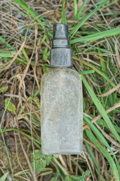 one gray dirty small plastic bottle with a black spray bottle lies on the ground in the green grass on the street