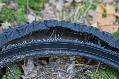 Siyah, eski, yırtık bir bisiklet lastiğinin parçası. Sokakta yerde bir delik var.