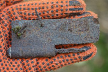 Turuncu iş eldivenindeki bir el eski kahverengi paslı demir kapı menteşesini sokakta tutuyor.
