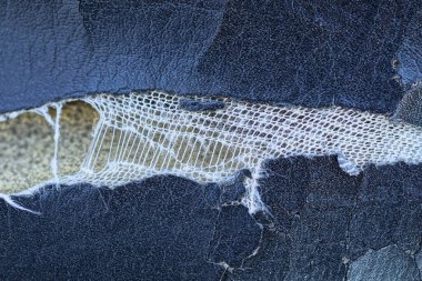 Siyah deri parçasında çatlaklar olan beyaz yırtık bir delik.