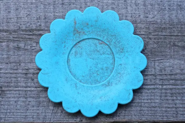 one small round dirty plastic plate toy stands on a gray wooden table
