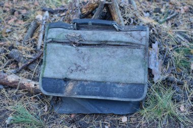 Eski, siyah, kirli, siyah bir evrak çantası sokakta duruyor.