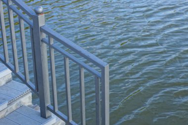 gray metal handrails and iron steps on the shore near the water of a reservoir on the street