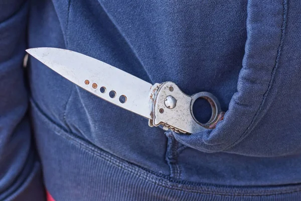 Beyaz keskin bıçaklı açık gri bir bıçak mavi bir elbise cebinde yatıyor.