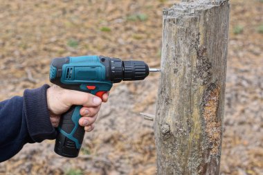 Tornavidayla çalışan bir işçi sokakta gri bir tahta kazık deliyor.