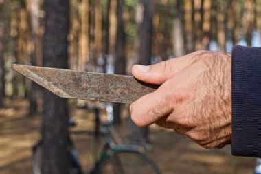 Mavi elbiseli bir adamın elinde gri, paslı bir bıçak var.