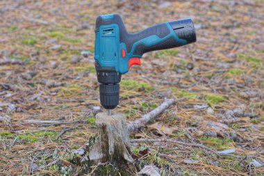 Bir renkli tornavida. Sokakta gri bir kütüğe elektrikli matkap saplanıyor.