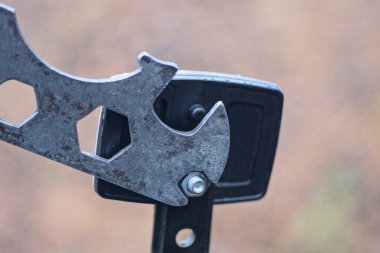 Eski gri bir demir alet, küçük bir somunu siyah plastik bir reflektörden bisiklete sıkıyor.