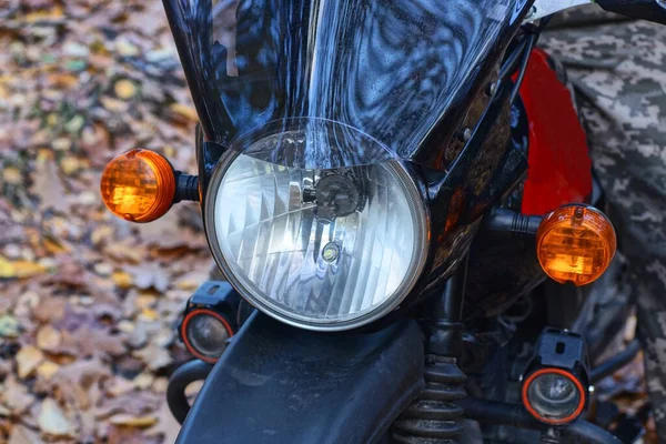 part of one black motorcycle with a white glass round headlight above the wheel on the street