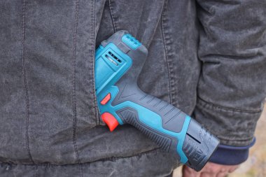 Bir elektrikli tornavida, sokakta çalışan bir işçinin gri ceketinin cebinde yatıyor.