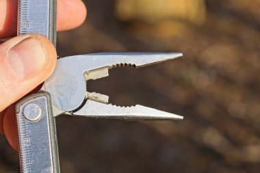 Kahverengi arkaplanda çok araçlı gri metal pense tutan eller