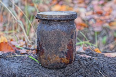 Eski, kirli, kapağı kapalı cam bir kavanoz. Sokakta gri zeminde duruyor.