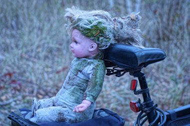 Eski, kirli bir oyuncak bebek akşam caddesinde siyah bir bisikletin bagajında oturuyor.