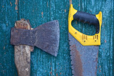 büyük eski bir balta ve paslı bir demir testeresi yeşil ahşap bir duvara karşı