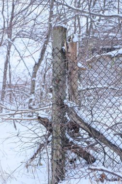 Dikenli telleri olan gri beton bir sütundan yapılmış eski bir çitin parçası. Ve kış sokağında beyaz bir kardaki metal ağ.
