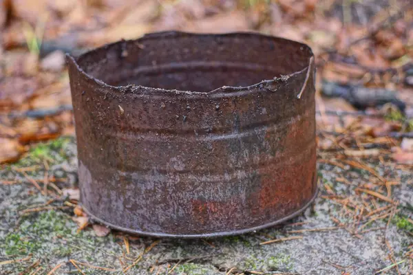 Kahverengi, yuvarlak, paslı demir bir teneke kutu sokakta yerde yatıyor.