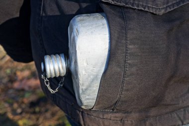 Siyah ceketin cebinde beyaz, eski bir alüminyum matara.