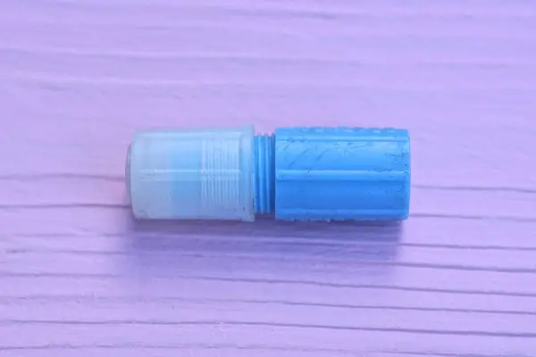 one small blue medical plastic tube with a white cap lies on a pink wooden table