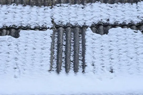 texture of gray slate on the roof of a house in white snow on a winter street