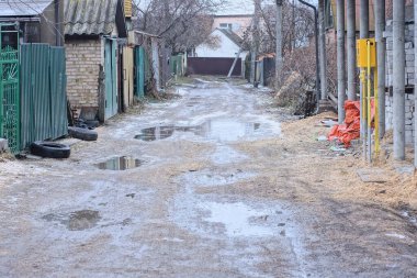 Gri kırsal bir yolun bir parçası. Sokaktan su birikintileri ve çukurlarla kaplı.