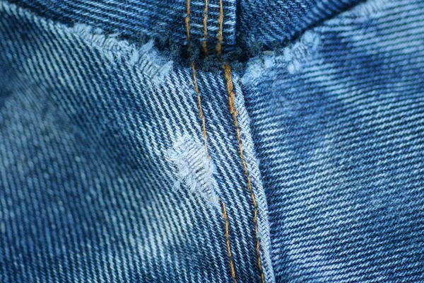 a piece of blue denim pants with white threads on torn fabric jeans